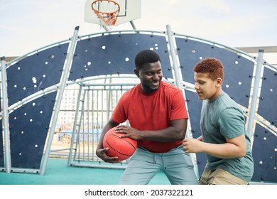 Teenage boy grabbing basketball from father while they playing together on sports ground