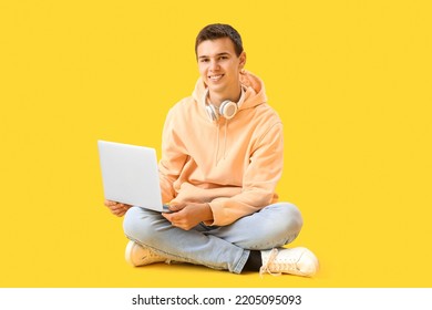 Teenage boy with headphones and laptop on yellow background - Powered by Shutterstock