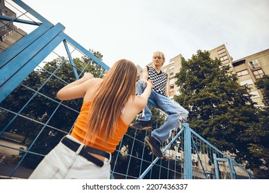 A teenage boy is helping his girlfriend climb up the railing in the urban exterior. - Shutterstock ID 2207436337