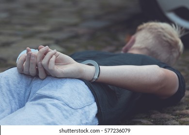 Teenage Boy With His Hands Cuffed Behind His Back Lying On The Ground Near A Car After Being Apprehended For A Misdemeanor Or Crime With Focus To His Hands