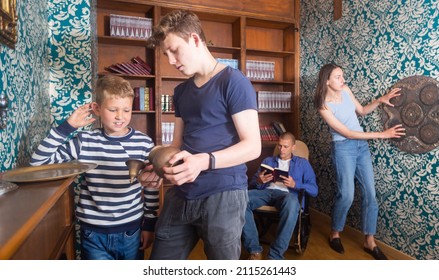 Teenage Boy And His Younger Brother Spending Time With Parents In Quest Room Designed As Old Library, Examining Ancient Kettle To Find Clue