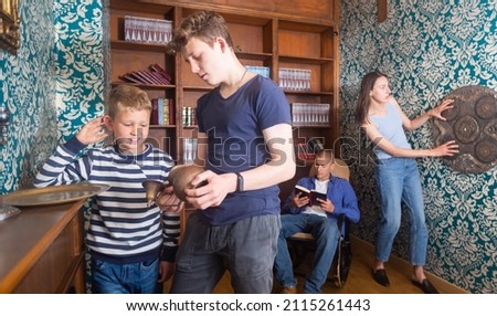 Teenage boy and his younger brother spending time with parents in quest room designed as old library, examining ancient kettle to find clue