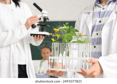 Teenage boy holding test tubes with plants in Biology class at school, closeup - Powered by Shutterstock