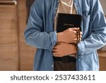 Teenage boy with Holy Bible and prayer beads in bedroom, closeup