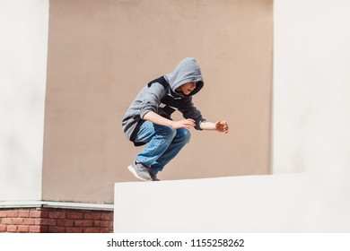 Teenage Boy In The Hood On A Street In A Big City Next To A High-rise Building Alone. Concept Of A Teenager Parkour Life. Parkour Jump Portrait On The Street In The Big City Close Up View