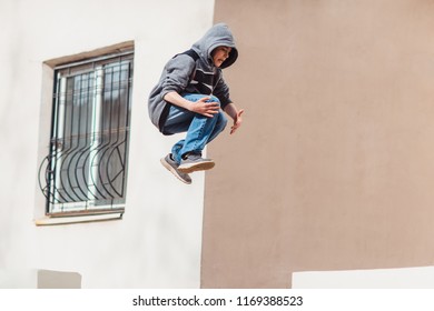 Teenage Boy In The Hood On A Street In A Big City Next To A High-rise Building Alone. Concept Of A Teenager Parkour Life. Parkour Jump Portrait On The Street In The Big City Close