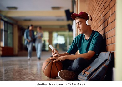 Teenage boy listening music on headphones while using mobile phone in high school hallway. Copy space. - Powered by Shutterstock