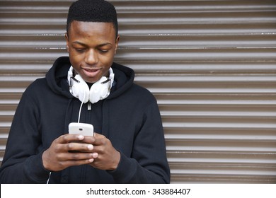 Teenage Boy Listening To Music And Using Phone In Urban Setting