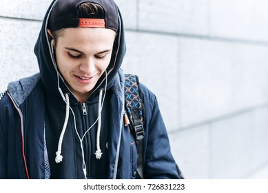 Teenage Boy Listening To Music And Using Phone In Urban Setting