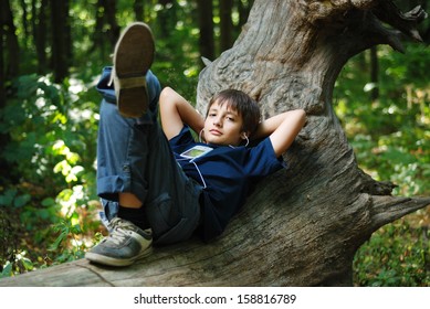 Teenage boy is lying on trunk and listening to music. Gadget is on his chest. Small earphones is in his ears. Green forest is full of sunlight and blurred. - Shutterstock ID 158816789