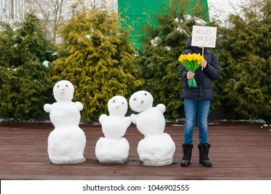 A teenage boy make snowmen. The concept of "hello spring." Spring came. In the hands of a snowman there are tulips and a sign with an inscription. Snow is melting. March.
