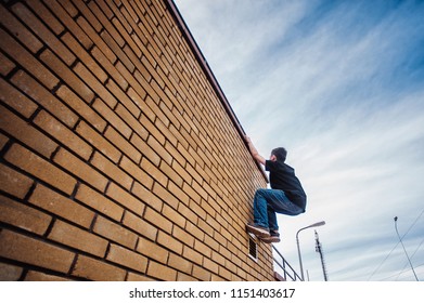 Teenage Boy On A Street In A Big City Next To A High-rise Building Alone. Concept Of A Teenager Parkour Life. Young Guy Climbs The Wall Close