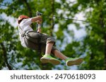 Teenage boy on zipline having fun at outdoor extreme adventure park. Active childhood, playing outdoors.