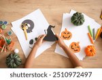 Teenage boy with paper witch hat making Halloween decorations on table, top view