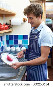 Teenage Boy With Part Time Job Washing Up In Coffee Shop