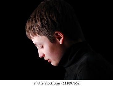 Teenage boy is photographed in profile on the black background. He is upset and his head are hung. She is wearing in black. - Shutterstock ID 111897662