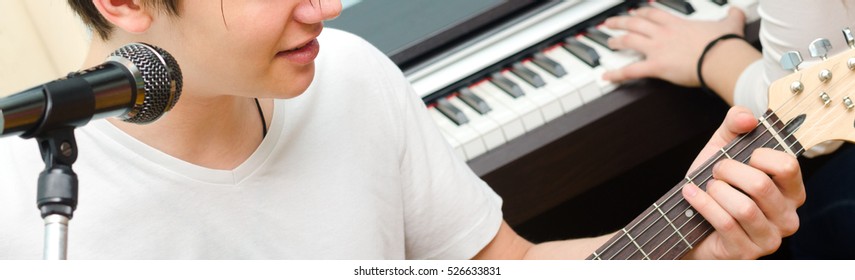 Teenage boy playing electric guitar and singing while girl plays on piano. - Powered by Shutterstock