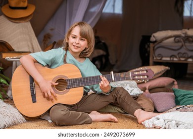 A teenage boy plays the guitar in a tent. Active children's recreation in nature. Learning to play the guitar. - Powered by Shutterstock