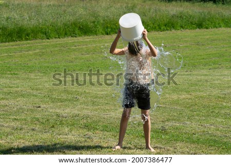 Teenage boy pouring bucket of cold water over his head outdoors. Ice water challenge. Cold water therapy benefits
