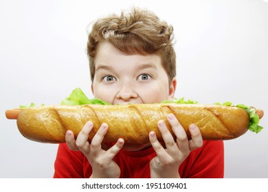 A Teenage Boy Is Raised To His Mouth And Bites Off A Huge Hot Dog On A Light Background. Fast Food Concept. National Hot Dog Day. Hot Dog Eating Championship. Copyspace.