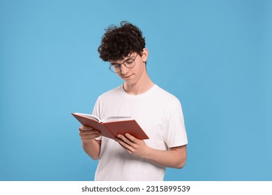 Teenage boy reading book on light blue background