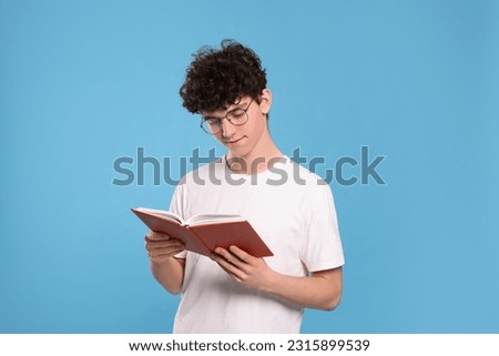 Teenage boy reading book on light blue background