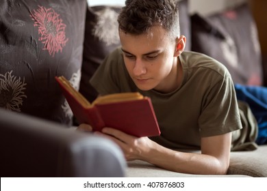 Teenage boy reading a book while laying on a sofa