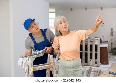 Teenage Boy Repair Worker And Disgruntled Mature Woman Homeowner Discussing Process Of House Renovation. Grandson Helping Grandmother With Home Improvement