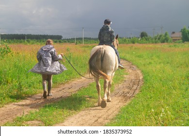 A Teenage Boy Riding A Horse, A Female Trainer Leads A Horse On A Cord In A Field. Teaching A Child To Ride In The Summer, Autumn Or Spring In The Meadow.