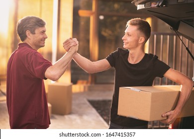 Teenage boy shaking hands with his father while moving into their new home together, carrying cardboard boxes. Single parent concept - Shutterstock ID 1647415357