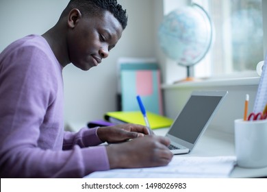 Teenage Boy Sitting At Desk Doing Homework Assignment On Laptop