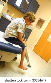 Teenage boy sitting on an examining table holding his crutches as he awaits the doctor's arrival.