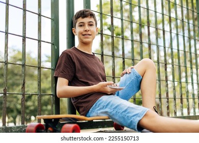 A teenage boy is sitting on a skateboard in the park and smiling - Powered by Shutterstock