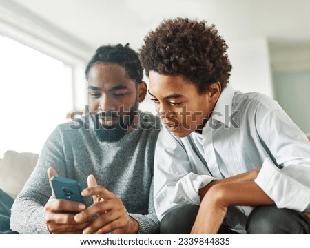 Teenage boy sitting at sofa with his father and using phone. Father and son bonding and having fun at home 