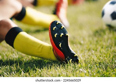 Teenage Boy Sitting and Stretching on Sports Grass Field. Soccer Ball in Background. Young Player Wearing Football Clothing and Soccer Cleats - Powered by Shutterstock