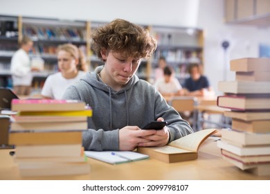 Teenage boy sitting at table and using smartphone in library. - Powered by Shutterstock