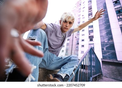 A teenage boy is sitting in an urban exterior surrounded by buildings. - Shutterstock ID 2207452709