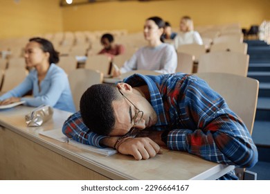 Teenage boy sleeping at desk during lecture with other students sitting in background - Powered by Shutterstock