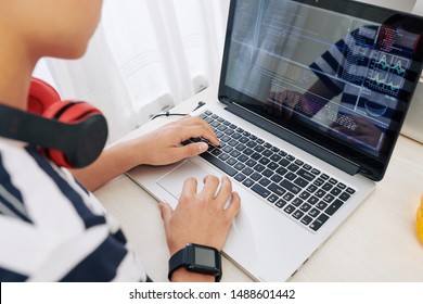Teenage boy with smartwatch and heaphones programming on laptop, he is testing new software he created