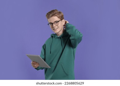 Teenage boy in stylish eyeglasses using tablet on purple background - Powered by Shutterstock