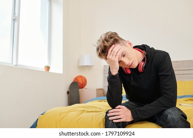 Teenage Boy Suffering From Severe Headache Sitting On Edge Of His Bed