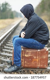 Teenage boy with a suitcase on the railway in rainy day 