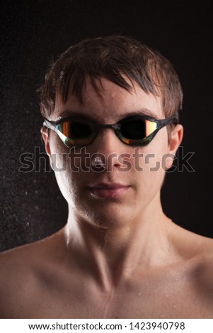 Teenage boy swimmer wearing swimming goggles with water spray.