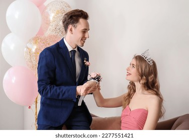 Teenage boy tying corsage around his girlfriend's wrist for prom in room