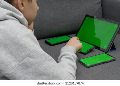 Teenage boy using multiple electronic internet devices in same time. Kid watching something on digital tablet, playing on cell phones at home. Multi screening, engaging in multiple gadgets at once - Shutterstock ID 2128159874