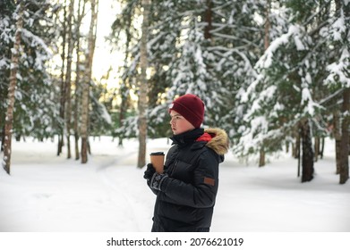 A teenage boy walks through a snow-kept park on a cold sunny day with a glass of hot drink in his hands. Winter walks.
