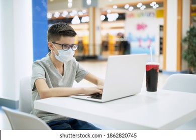 Teenage Boy Wearing Face Mask Uses A Laptop While Sitting At Food Court