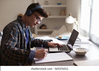 Teenage boy wearing headphones works at desk in his bedroom