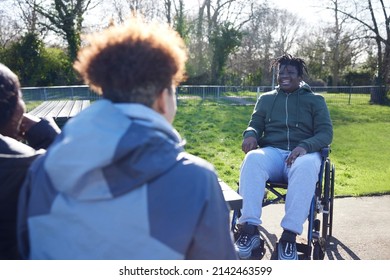 Teenage Boy In Wheelchair Hanging Out Talking And Laughing With Friends In Park 