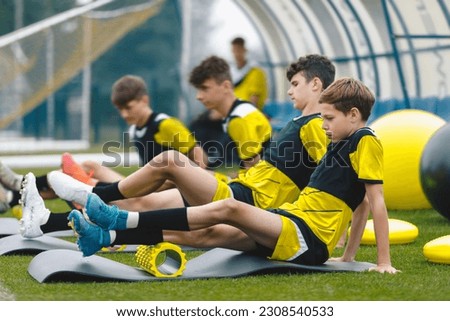 Teenage boys at football training in soccer club. Sports summer camp for youth footballers. Boys using foam therapy rollers after training session outdoor
